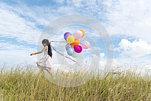 Happy woman jumping with air balloons on the meadow