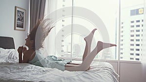 Happy woman jumping on bed at home and relaxing by the panoramic window with amazing city view