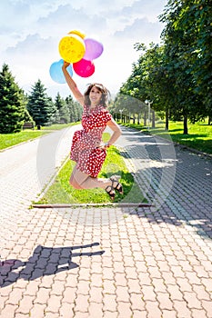 Happy woman jumping with colored balloons in the park