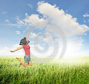 Happy Woman jumping in green grass fields with clouds sky