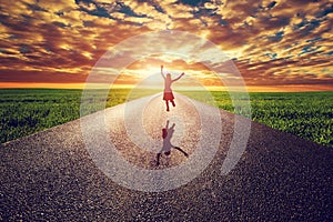 Happy woman jumping on long straight road, way towards sunset sun