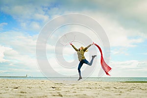 Happy woman jumping with scarf on beach