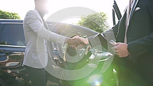 Happy woman keeping a key sitting in car`s interior and men shaking hands entering into an acquisition agreement