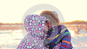 Happy woman kisses her child in a winter park against a sunset background