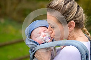 Happy woman kissing her baby while holding and carrying it in a baby carrier