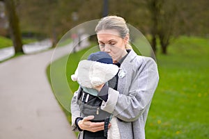 Happy woman kissing her baby that she is holding and carrying in a baby carrier