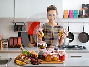 Happy woman in kitchen holding jars of preserved vegetables