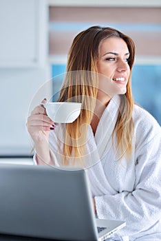 Happy woman in the kitchen reading he news on her laptop