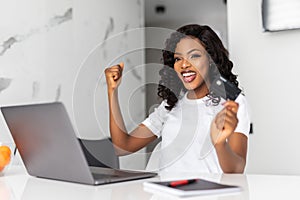 Happy woman with laptop with win gesture, credit cards and shopping bags at home