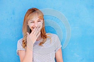 Happy woman laughing with hand to mouth against blue wall