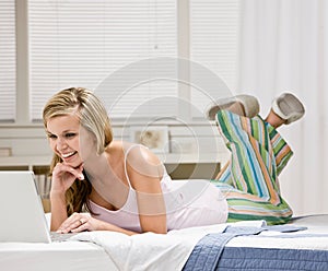 Happy woman laying on bed in bedroom using laptop