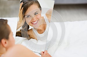 Happy woman laying on bed and looking on mirror