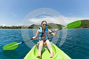 Happy woman with lifejacket kayaking in tropical island ocean on vacation.