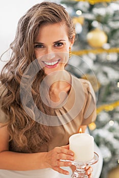 Happy woman lighting candle near christmas tree