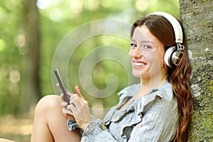 Happy woman listening music looks at you in a forest