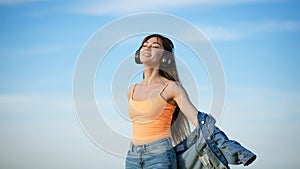 Happy woman listening to music with headphones and dancing in nature against the sky