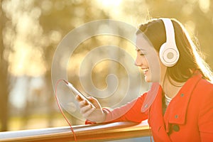 Happy woman listens music on phone in a balcony at sunset