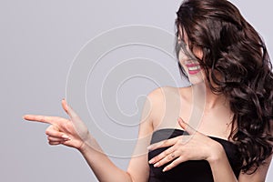 Happy woman with long and shiny wavy hair . Beautiful model, curly hairstyle on gray background showing on copy space.