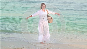 Happy woman in the long white dress spinning and dancing at the ocean sea beach