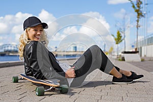 Happy woman with longboard sitting on the ground