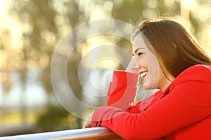 Happy woman looking away in a balcony at sunset