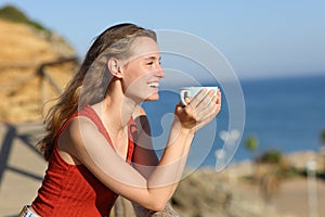 Happy woman looking away on the beach holding coffee