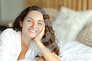 Happy woman looking at camera on a bed smiling