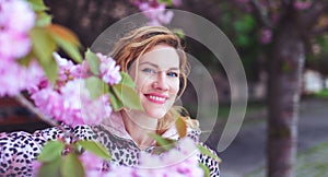 Happy woman looking into camera in park during cherry tree blooming photo