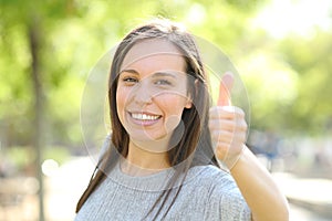 Happy woman looking at camera with thumbs up in a park