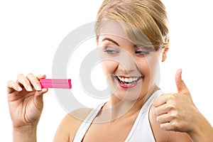 Happy woman looking at pregnancy test with positive result and showing thumbs up