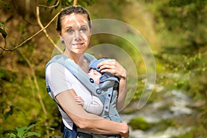 Happy woman looking to camera while holding and carrying it in a baby carrier photo