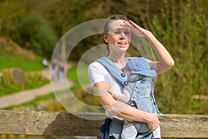 Happy woman looking to distance with hand on forehead while holding her baby photo