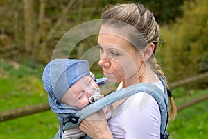 Happy woman looking to her baby while holding and carrying it in a baby carrier