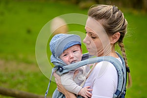 Happy woman looking to her crying baby while holding and carrying it in a baby carrier photo