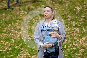 Happy woman looking to side while holding and carrying it in a baby carrier photo