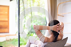 Happy woman looking on window while sitting on couch in living room with hands over head,Relax time