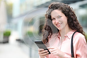 Happy woman looks at you holding mobile phone