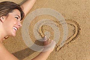 Happy woman in love drawing a heart on the sand of the beach