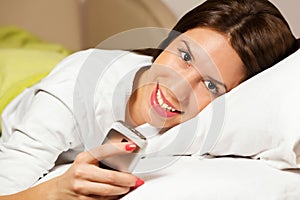Happy woman lying on bed smiling, reading a text message