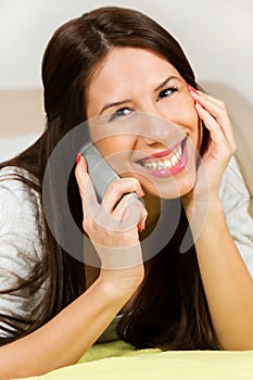 Happy woman lying on bed smiling, talking on her cellphone