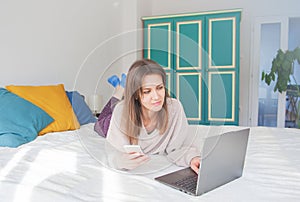 Happy woman lying down on the bed and working with computer at home