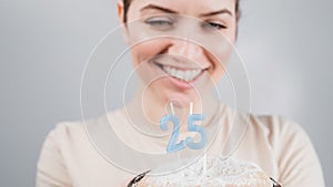 The happy woman makes a wish and blows out the candles on the 25th birthday cake. Girl celebrating birthday.