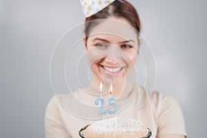 The happy woman makes a wish and blows out the candles on the 25th birthday cake. Girl celebrating birthday.