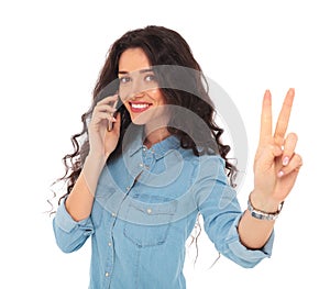 Happy woman making victory sign while talking on the phone