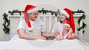 Happy woman and man with baby on bed decorated for Christmas