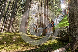 Happy woman man couple relaxing in hanging tent camping in forest woods during sunny day.Group of friends people summer