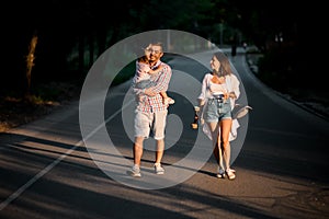 Happy woman and man with little child are walking in the evening park