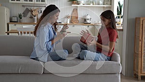 Happy woman millenial and teenage girl are sits on sofa and exchanging gifts for family holiday