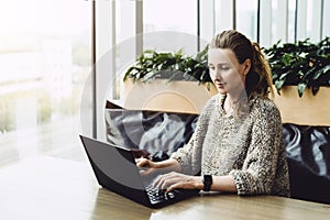 Happy woman millennial using laptop while sitting at cafe.Young businesswoman sitting in coffee shop,working on computer