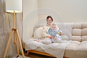 Happy woman mother with infant baby reading book on home sofa in living room